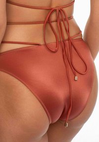 Rdzawopomarańczowe majtki bikini o gładkiej fakturze, wysokim kroju i regulowanymi bokami z elementami ze złotego metalu.