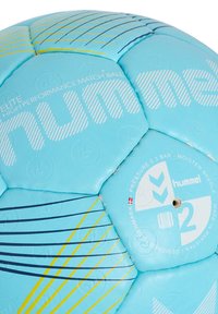 Ljusblå handboll med en hexagonal design, texturerad yta och flerfärgade ränder. "hummel"-logotypen tryckt framträdande på ytan.