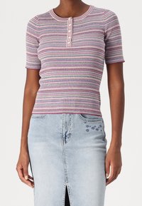 Femme portant un haut en tricot rayé à manches courtes ajusté avec des détails de boutons, associé à une jupe en denim légère ornée de petites fleurs brodées.