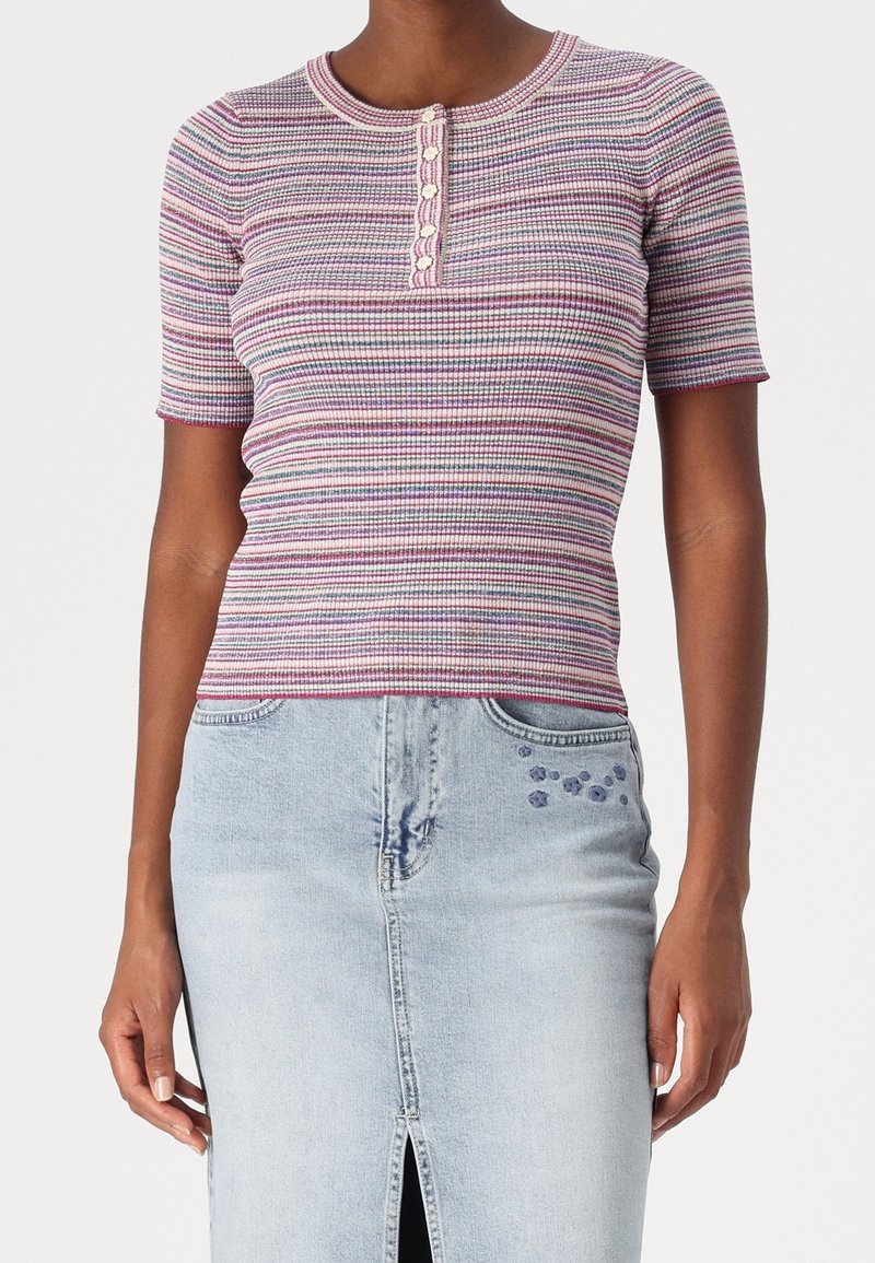 Femme portant un haut en tricot rayé à manches courtes ajusté avec des détails de boutons, associé à une jupe en denim légère ornée de petites fleurs brodées.