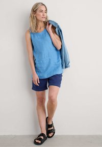 Světle modrý bezrukávový top s kulatým výstřihem, doplněný námořnickými šortkami. Černé sandály dokončují outfit. Ležérní džínová bunda přehozená přes rameno.