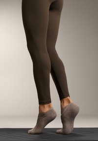 Smeđe tajice s prilagođenim krojem uparene sa svijetlosivim, pletenim čarapama protiv klizanja, s teksturiranom đonom i elastičnim remenom oko gležnja.