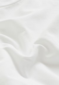 Weißer Stoff mit einer glatten, leicht strukturierten Oberfläche, die sanfte Falten und Knicke aufweist und ein lässiges, entspanntes Erscheinungsbild vermittelt.