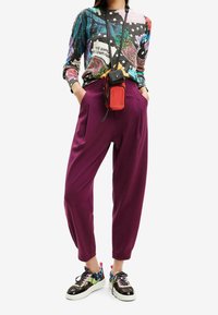 Pull graphique multicolore, pantalon taille haute violet foncé et baskets à motifs. Petit sac bandoulière rouge. Matériaux texturés.