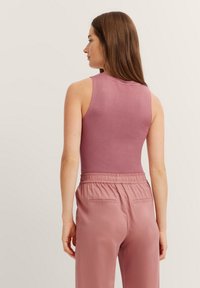 Fitted sleeveless top in soft, textured light pink material, paired with matching loose trousers featuring an elastic waistband and back pockets.