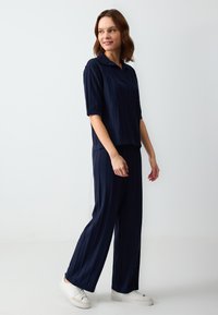Marineblaues Strick-Zweiteiler-Set mit kurzärmligem Polohemd und weit geschnittenen Hosen, die über eine vertikale Rippstruktur und subtile Designdetails verfügen.