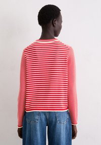 Gestreiftes Langarmshirt in Rot und Weiß mit Rundhalsausschnitt und gerippten Abschlüssen. Kombiniert mit lockeren blauen Jeans.