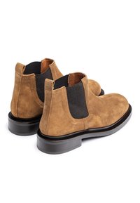 Brown suede Chelsea boots with black elastic side panels, round toe shape, and a black rubber sole. Smooth texture and simple design.