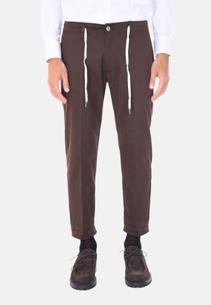 Pantaloni in cotone marrone con vestibilità affusolata, dotati di chiusura con bottone e lacci bianchi, orli arrotolati e decorazioni minime.