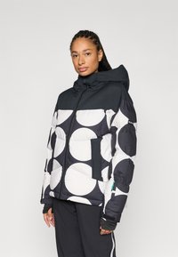 Zwart-wit donsjack met grote ronde patronen, voorzien van een capuchon, voorrits en zijzakken. Lichtgewicht, gewatteerd ontwerp.