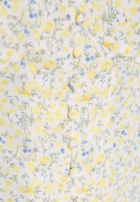 Tecido branco com um padrão floral, apresentando flores amarelas e azuis e caules verdes. Seis botões na frente, combinando com a textura do tecido.