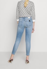 Jeans skinny de denim azul claro con cintura alta, bolsillos traseros y una etiqueta negra. Combinados con una blusa de mangas largas blanca y negra con estampado.