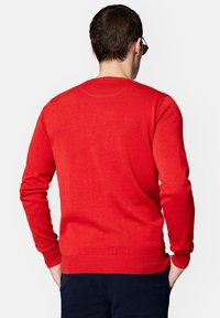 Czerwony sweter z okrągłym dekoltem, z długimi rękawami, wykonany z gładkiego dzianinowego materiału. Prążkowane mankiety i dół dodają tekstury. Prosty design, bez wzorów i akcentów.