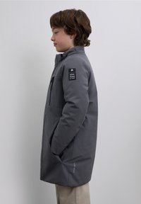 Gray insulated coat with a high collar, zippered front, side pockets, and a logo patch on the left sleeve. Smooth texture, casual design.