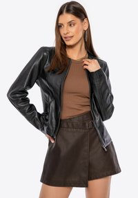 Black leather jacket with a fitted silhouette, featuring a zip closure and smooth texture. Paired with a brown ribbed top and dark brown skirt.