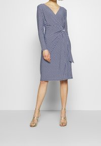 Abito avvolgente blu navy con maniche lunghe, caratterizzato da un motivo geometrico, dettaglio in vita arricciato e orlo fino al ginocchio.