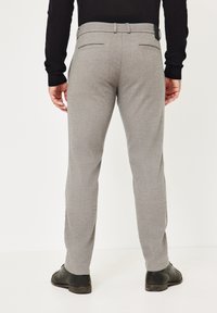 Grau maßgeschneiderte Hose mit glatter Textur, zwei Taschen und einem Bund mit Gürtelschlaufen. Trägt schwarze Schuhe.