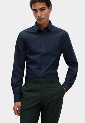 Donker marineblauwe langemouwen overhemd met een button-down kraag, gladde textuur en bijpassende knopen, gedragen met op maat gemaakte donkergroene broek.