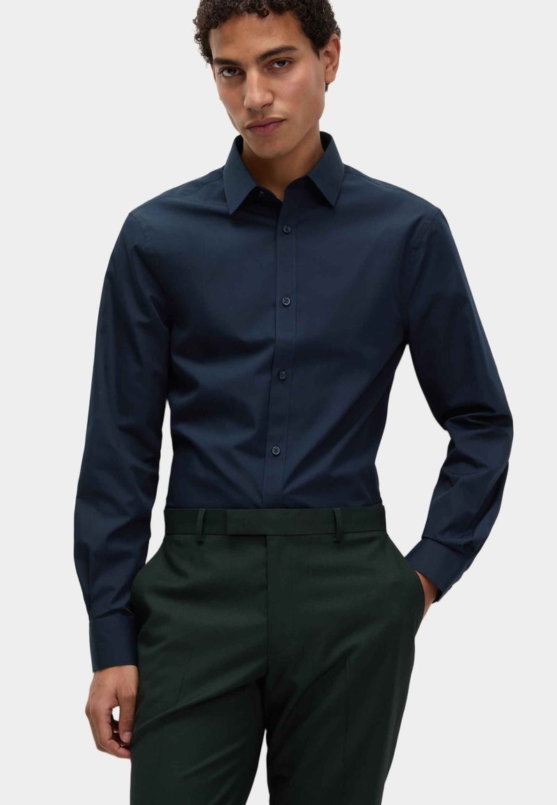 Donker marineblauwe langemouwen overhemd met een button-down kraag, gladde textuur en bijpassende knopen, gedragen met op maat gemaakte donkergroene broek.