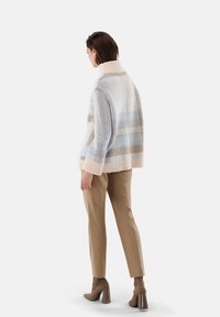 Strickpullover in sanften Pastellfarben mit horizontalen Streifen, hohem Kragen und gerippten Bündchen, kombiniert mit beigen, enganliegenden Hosen und hohen Stiefeln.