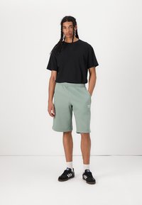 Μαύρη κοντομάνικη μπλούζα και ανοιχτό πράσινο σορτς από μαλακό ύφασμα, με ελαστική μέση και μικρό λογότυπο στο σορτσάκι.