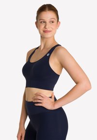 Granatowy stanik sportowy wykonany z gładkiego materiału o designie z plecami w stylu racerback; posiada logo na lewym ramieniu i dopasowany krój.