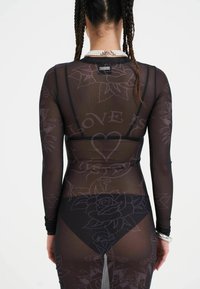 Schwarze, transparente Longsleeve-Bluse mit Blumen- und Textmustern, im taillierten Design und einem festen schwarzen unteren Teil, der durch den Stoff hindurch sichtbar ist.