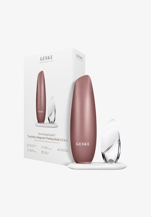 Set GESKE SmartAppGuided Touchless Magnetic Peeling Mask avec un appareil couleur or rose et un outil transparent semblable à un cristal sur une base blanche à côté de la boîte du produit.