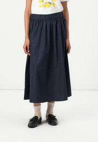 Marineblaue Baumwollrock mit gerafftem Bund, fließender Silhouette, sauber verarbeitetem Saum, kombiniert mit beigen Socken und schwarzen Schuhen.