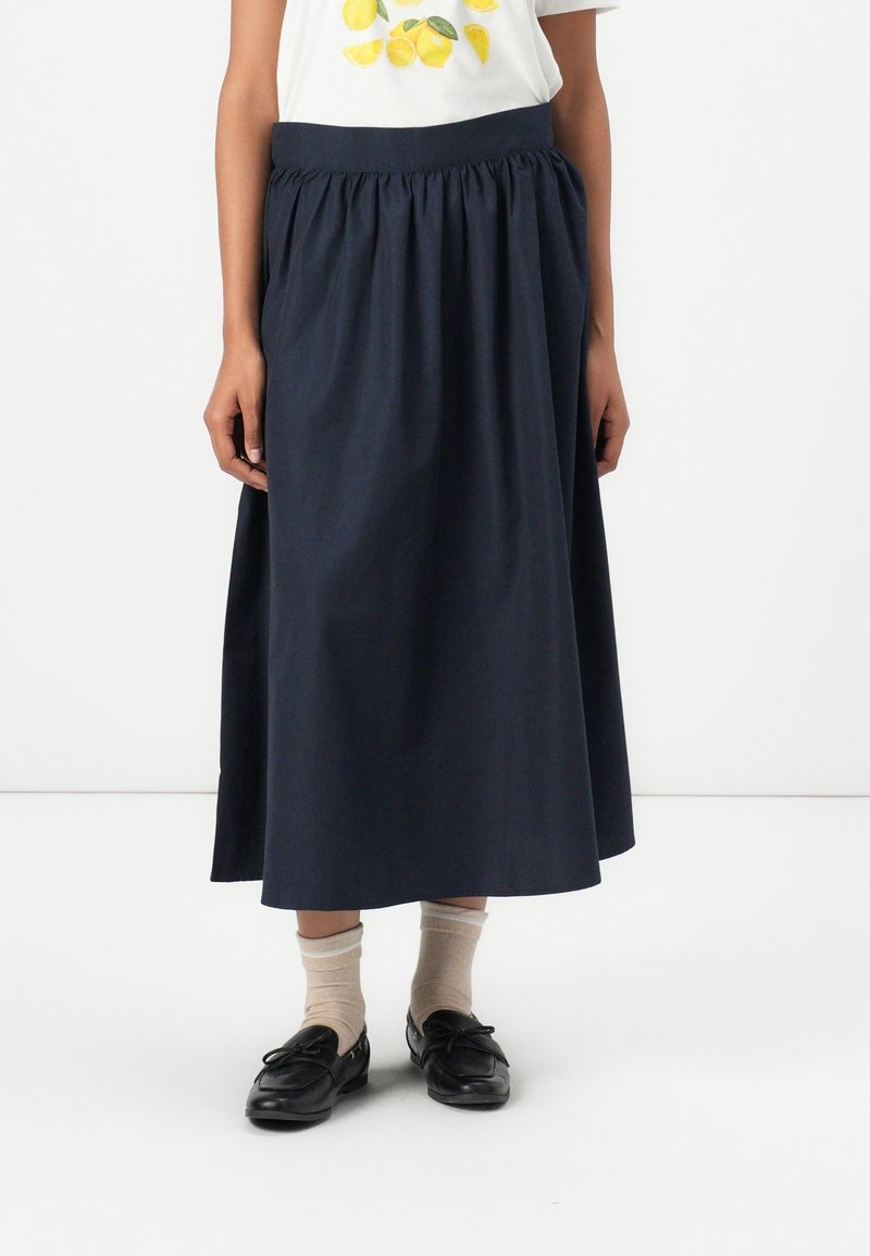 Marineblaue Baumwollrock mit gerafftem Bund, fließender Silhouette, sauber verarbeitetem Saum, kombiniert mit beigen Socken und schwarzen Schuhen.