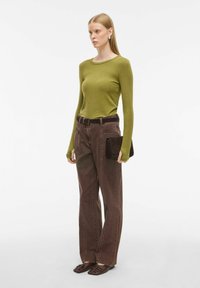 Dolga majica, prilagojena olivno zelena barva, v kombinaciji z visokim pasom, rjavimi kordnim hlačami. Dodatki vključujejo temno rjavo torbico in temne čevlje.