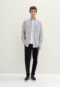 Camisa a rayas de botón con un bolsillo en el pecho, combinada con pantalones negros y zapatillas grises. Tejido suave con un corte relajado.