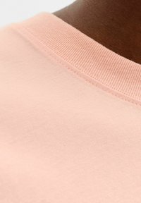 Kerge roosa puuvillane kangas ribitud ümarate kaelustega. Tekstuur on sile, näidates peeneid õmblusi ääredel.