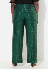 Groene paillettenwijde pijpen met een schitterende textuur. Heeft een hoge taille en is gecombineerd met zwarte hakken, gezien vanaf de achterkant.