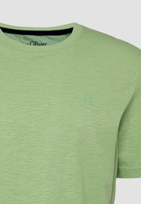 T-shirt vert clair à manches courtes et col rond avec un tissu subtilement texturé et un petit logo embossé sur la poitrine gauche.