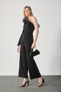Combinaison noire avec une manche longue et des volants transparents. Portée avec des sandales à talons noirs et un sac noir plissé.
