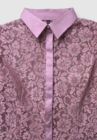 Spitzenbluse in sanftem Pink mit Satin-Kragen und Knopfleiste. Blumendesign auf dem gesamten Stoff, das die filigrane Spitzenstruktur zeigt.