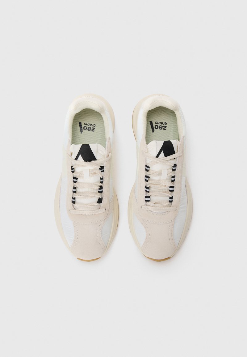 Beige Sport- und Freizeitschuhe aus einer Kombination von Wildleder und Mesh-Materialien, mit schwarzen Schnürsenkeln, runder Zehenform und einer leichten Gummisohle.