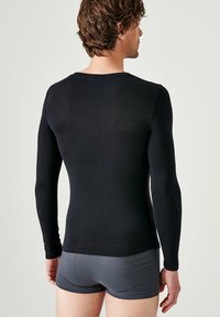 Black long-sleeve shirt made from a soft, stretchy material. Features a round neck and fitted design, paired with grey shorts.