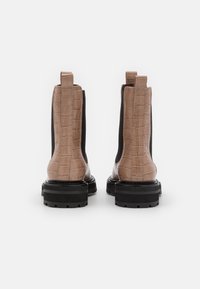 Bottines en cuir beige embossé crocodile avec des panneaux élastiques latéraux noirs et des semelles en caoutchouc noir épaisses. Présente des languettes de talon en boucle pour un enfilage facile.