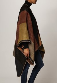 Multicolored poncho featuring a blend of brown, green, and black wool. Edged with decorative stitching. Oversized, relaxed fit.