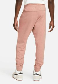 Pink cotton sweatpants with a tapered design, elastic waistband, and speckled texture, paired with white and gray sneakers.