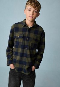 Groene en marineblauwe geruite overhemd met lange mouwen, voorzien van twee borstzakken en knoopsluiting bij de manchetten, gemaakt van een zachte, gestructureerde stof. Zwarte jeans inbegrepen.