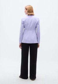 Λιλά ραμμένο σακάκι με μακριά μανίκια και γιακά με σχισμή, συνοδευόμενο από μαύρο παντελόνι φαρδιάς γραμμής. Λείο ύφασμα με εφαρμοστή σχεδίαση.