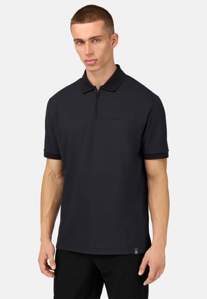 Polo negro de manga corta, con cuello con cremallera y un bolsillo en el pecho. Hecho de una tela suave con puños más oscuros en contraste y una sutil etiqueta de logo.