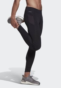 Black athletic leggings with a fitted design, featuring a textured pocket panel, and paired with grey running shoes.