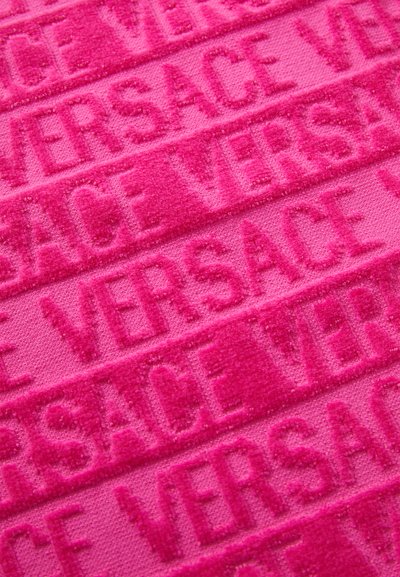 Tissu rose avec un texte « VERSACE » en relief, à la surface douce et texturée. Le motif de marque répété ajoute de la profondeur au design.