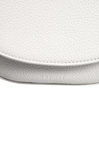 Bolso circular de cuero blanco con superficie texturizada, que cuenta con un fondo plano y el nombre de la marca en relieve en el lateral. Diseño pequeño y minimalista.