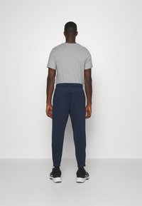 Grey short-sleeve t-shirt, navy sweatpants with elastic waistband, slim fit, side pockets, and ankle cuffs. Black athletic shoes.