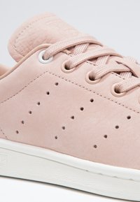 Nära bild av en ljusrosa mockasin sneaker med tonade snören, perforerad sidodetalj och en vit texturerad gummisula.